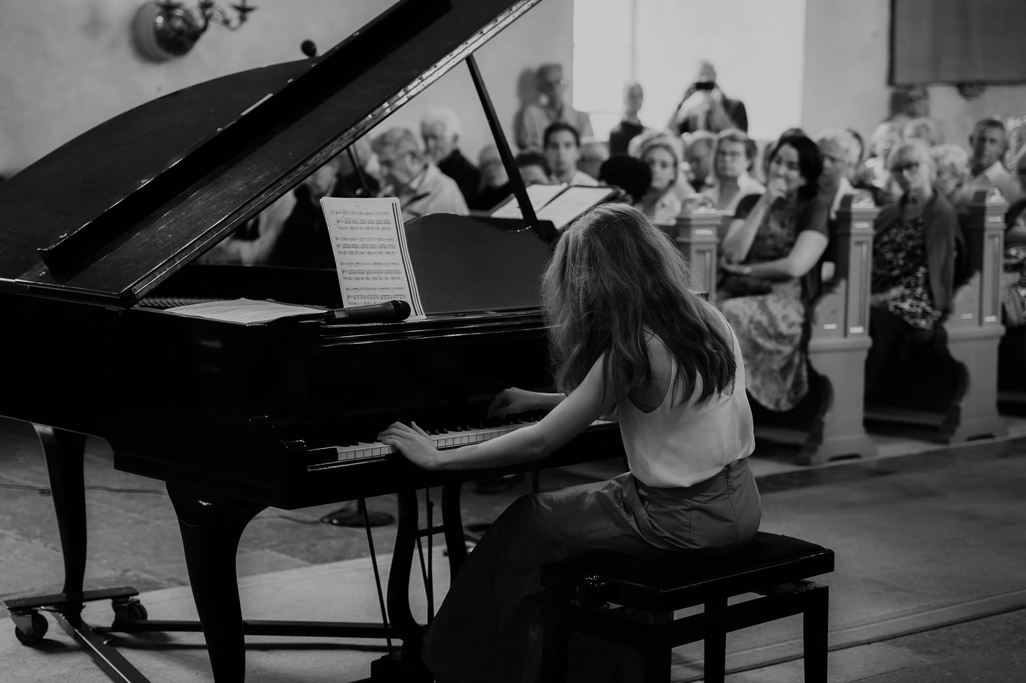 Alice is playing the grand piano and we can also see the audience